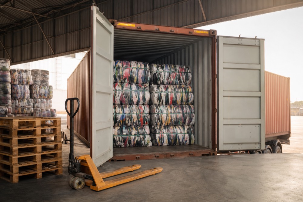 A shipping container being loaded with bales of used clothing for export